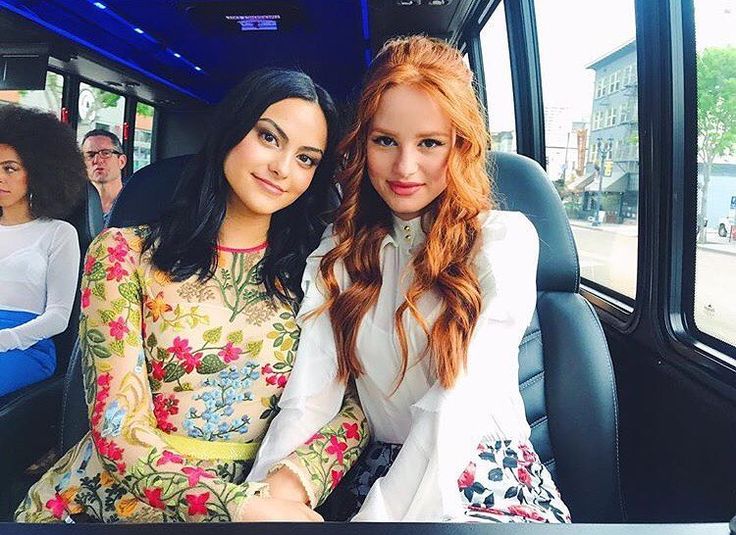 two beautiful young women sitting next to each other on a bus seat in front of a crowd