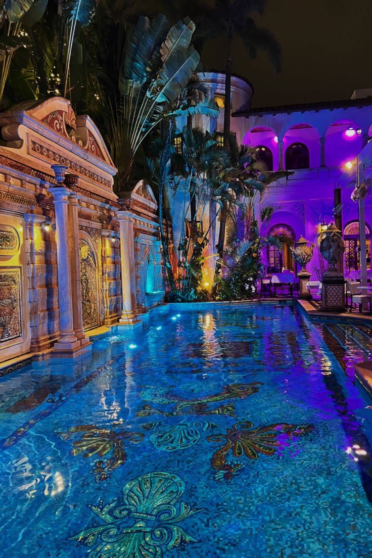 an indoor swimming pool surrounded by palm trees and blue lighting in the night time area