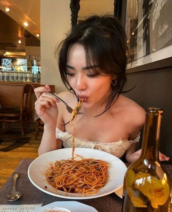 a woman is eating spaghetti from a white bowl