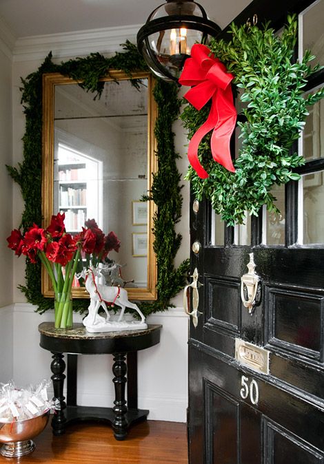 a black door with red flowers and greenery on the top, in front of a mirror