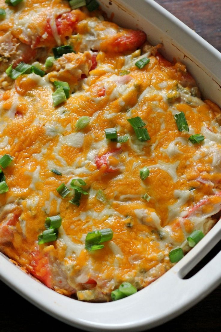 a casserole dish with cheese, green onions and tomatoes in it on a wooden table