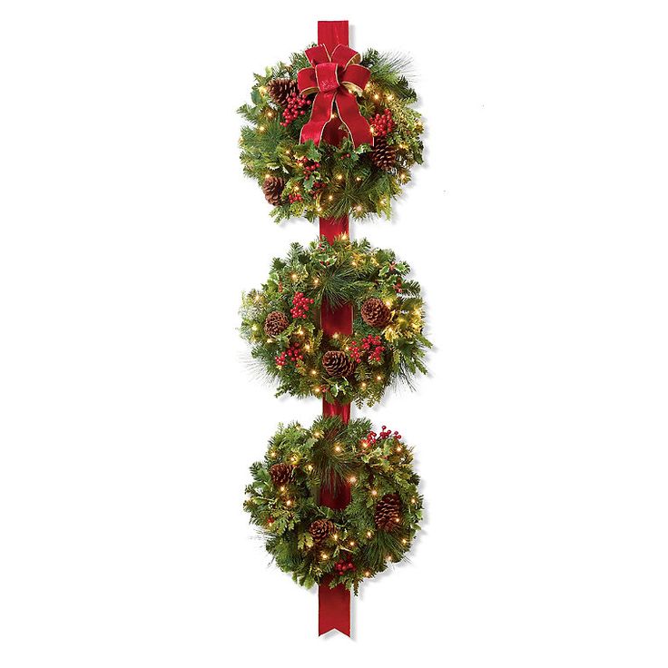 three christmas wreaths hanging on a pole with red bows and lights around the top