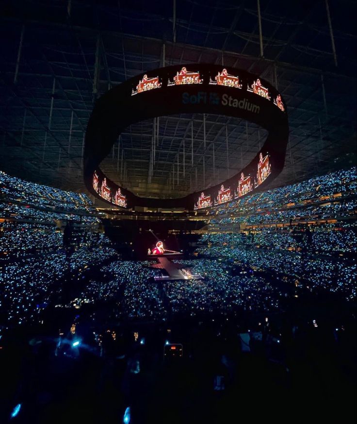 a large stadium filled with lots of people and lights on the side of it at night