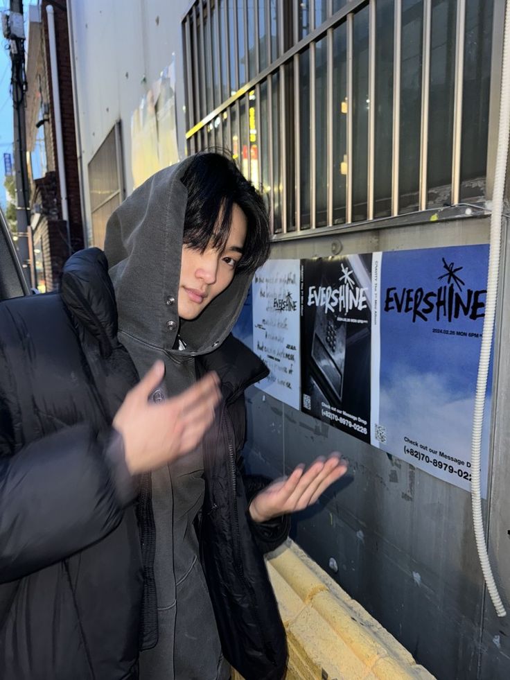 a man in a hooded jacket standing next to a wall