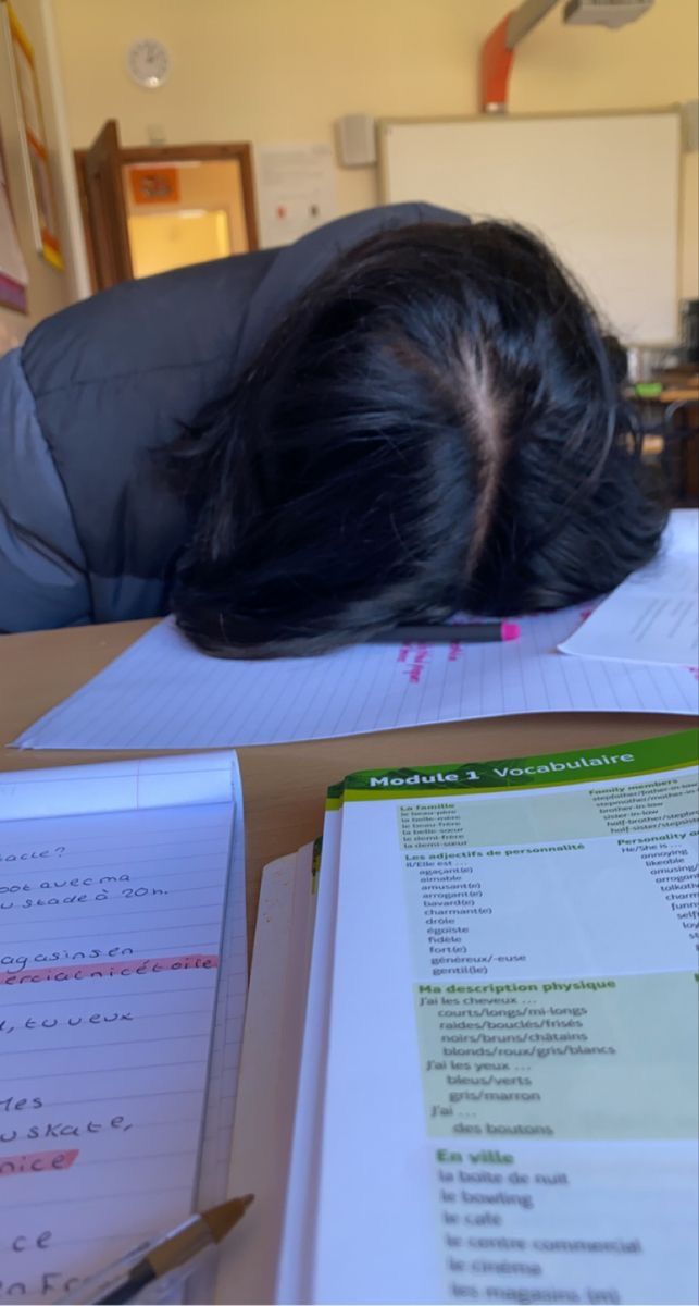 a person laying their head on top of a desk with papers and pens in front of them