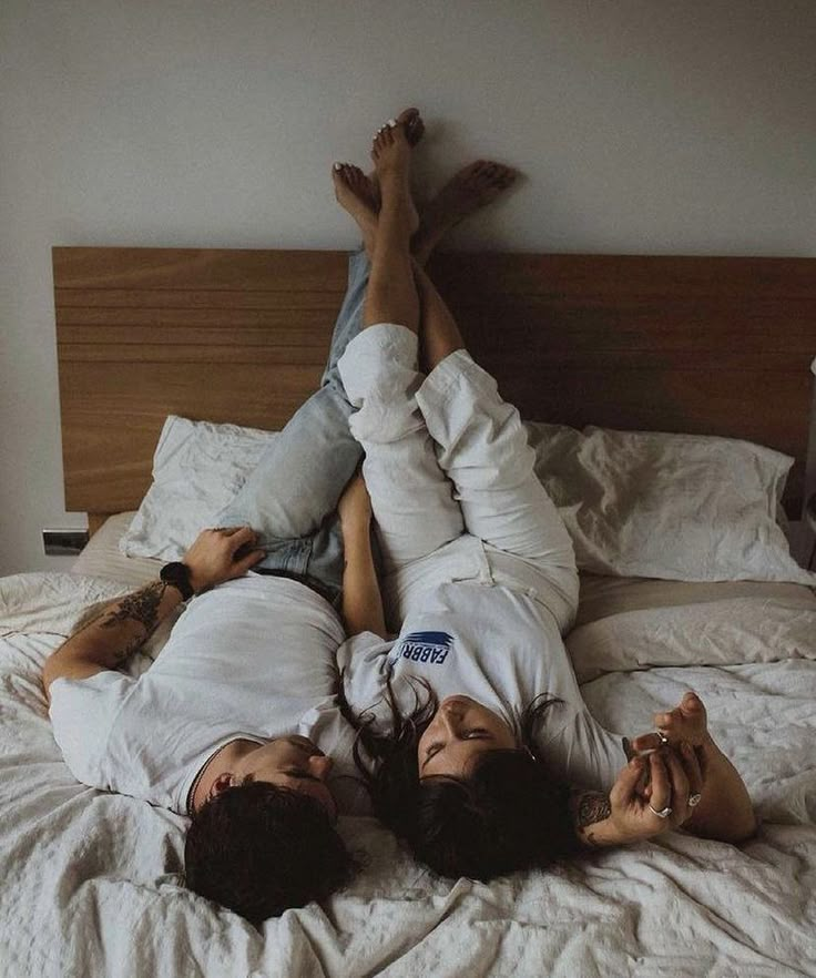 two people laying on a bed with white sheets