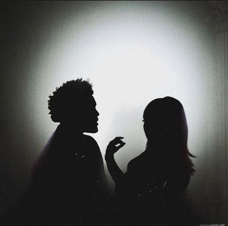 two women standing next to each other in front of a white wall with light coming from behind them