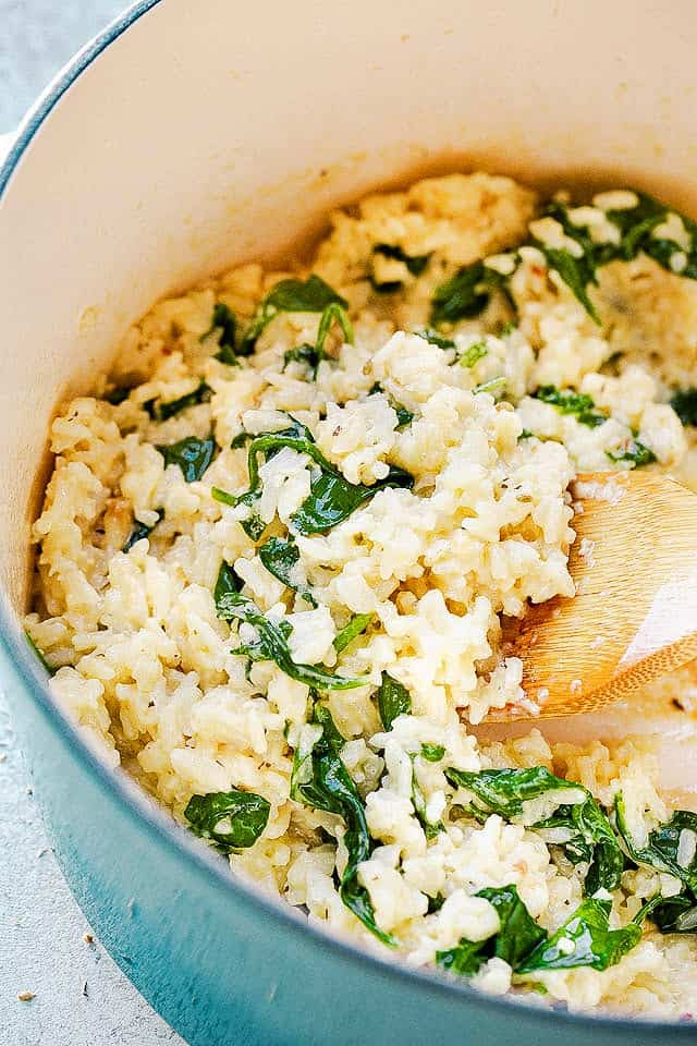 a pot filled with rice and spinach next to a wooden spoon