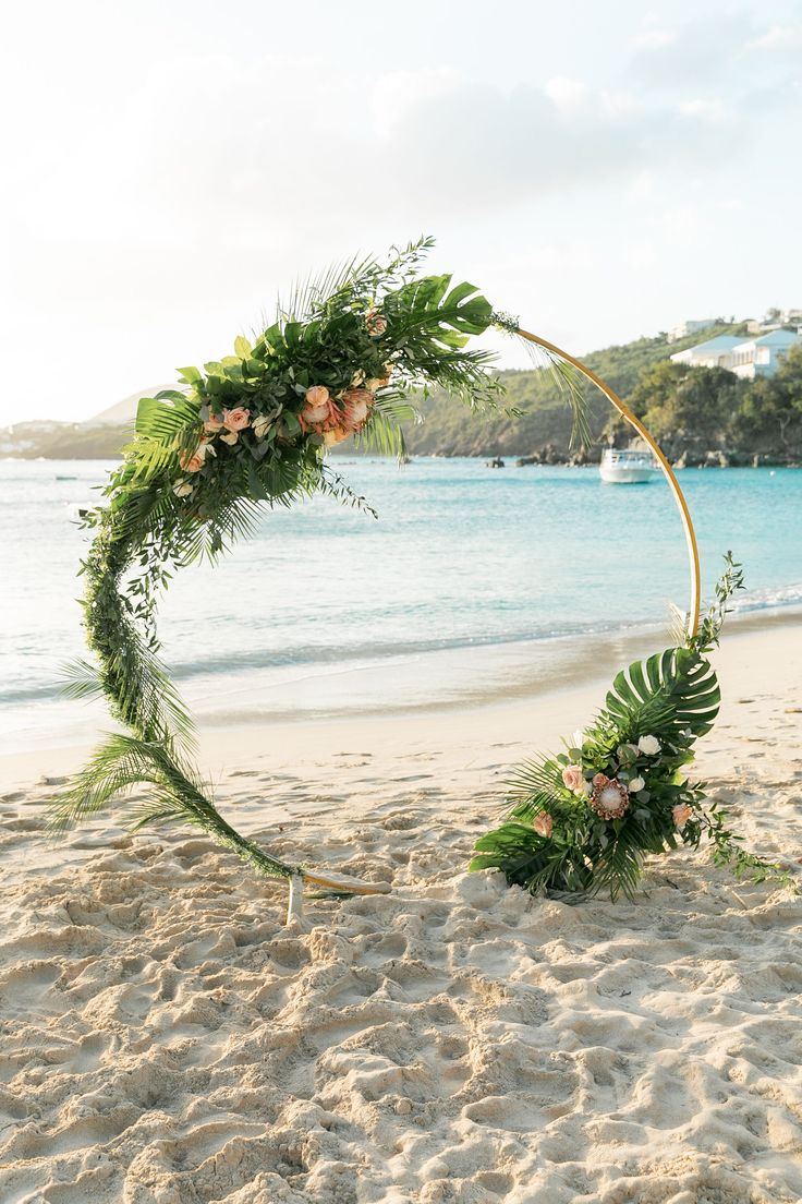 a wedding arch on the beach with flowers and greenery