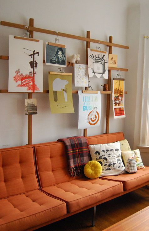 an orange couch sitting in front of a window next to a wooden shelf with pictures on it