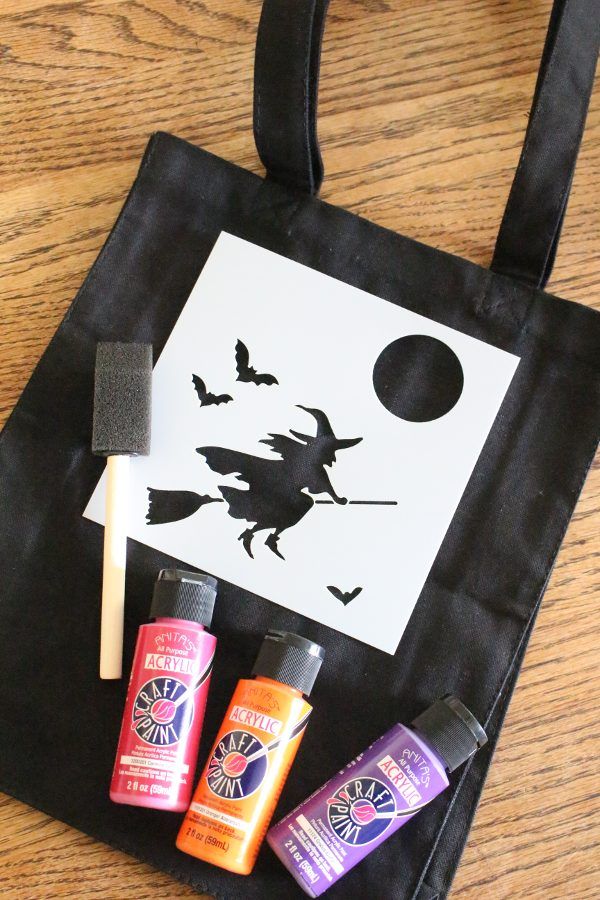 a black bag with three different items in it on top of a wooden table next to a paper cut out of a witch