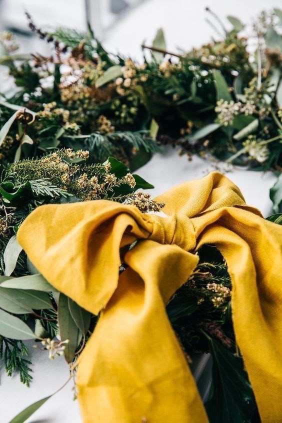 a yellow scarf tied to a wreath with greenery