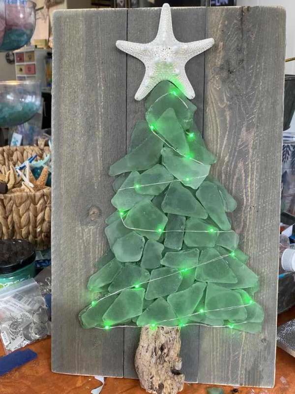 a christmas tree made out of sea glass is displayed on a wooden board with a starfish