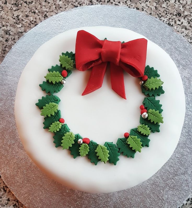 a decorated cake with holly and red bow on top is sitting on a countertop