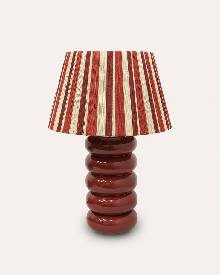 a lamp that is sitting on top of a white tablecloth with a red and white striped lampshade