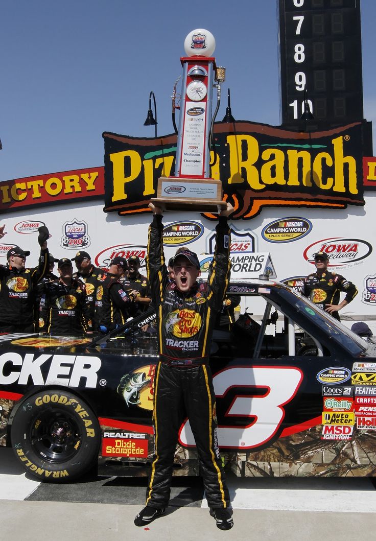 a man standing in front of a race car holding up a trophy on top of his head