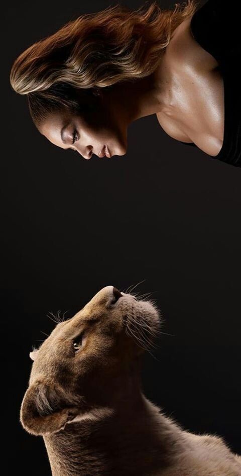 a woman standing next to a lion looking up at it's head in the air