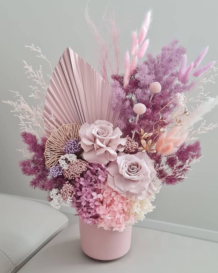 a pink vase filled with lots of different types of flowers next to a white wall