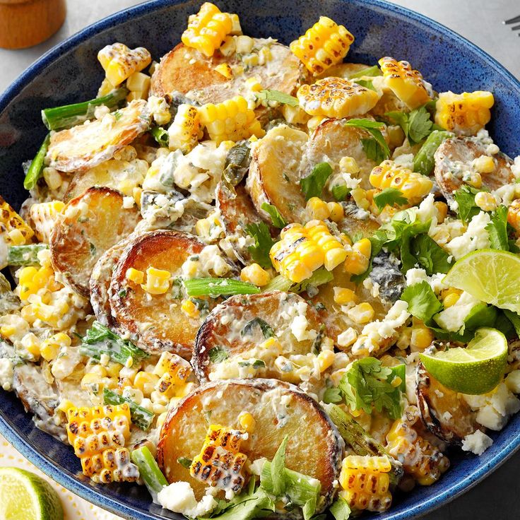 a blue bowl filled with corn and potato salad on top of a table next to lime wedges