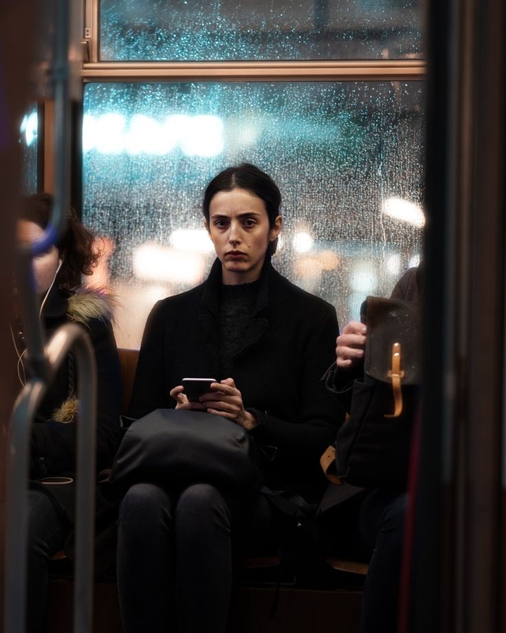 a woman sitting on a bus looking at her cell phone and holding something in her hand