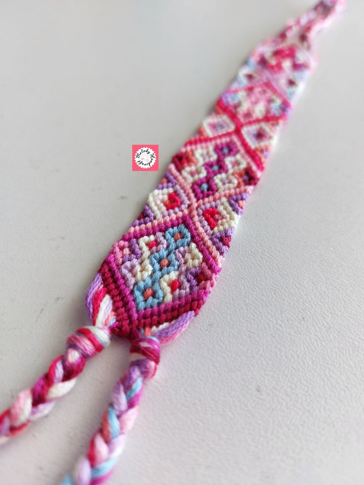 a pink and blue beaded bracelet laying on top of a white table next to a red button