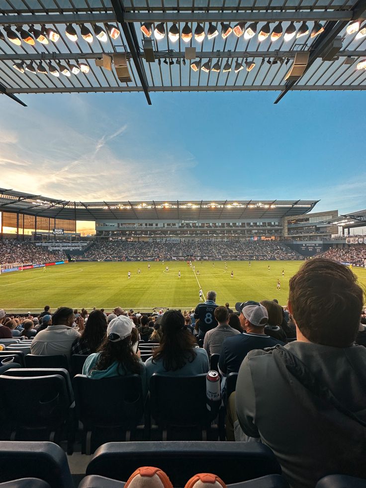 people are sitting in the stands watching a soccer game on a sunny day at a stadium