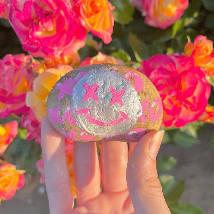 a hand holding a rock with the word love painted on it and flowers in the background