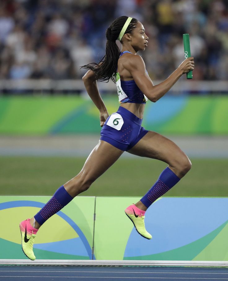 a woman running on a track with her leg in the air and holding a green stick