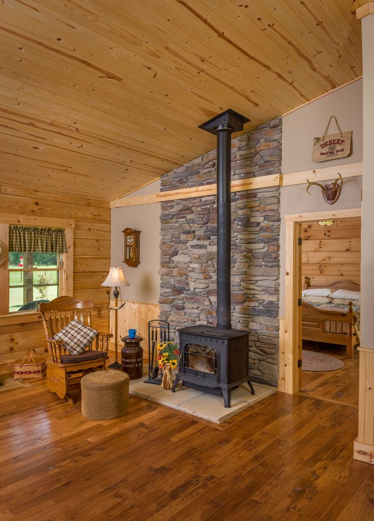 a living room with wood floors and a stone fireplace in the center, surrounded by wooden walls