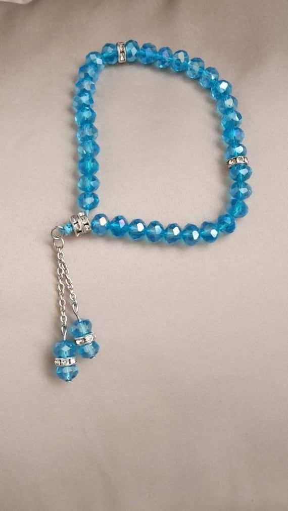 a blue beaded bracelet with a silver cross charm on the end and a chain attached to it