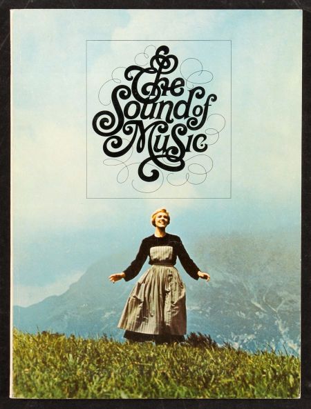 a woman standing on top of a grass covered hill next to a sign that says the sound of music