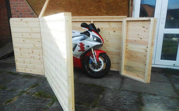 a motorcycle is parked in front of a wooden storage shed with its door open and the motorbike inside