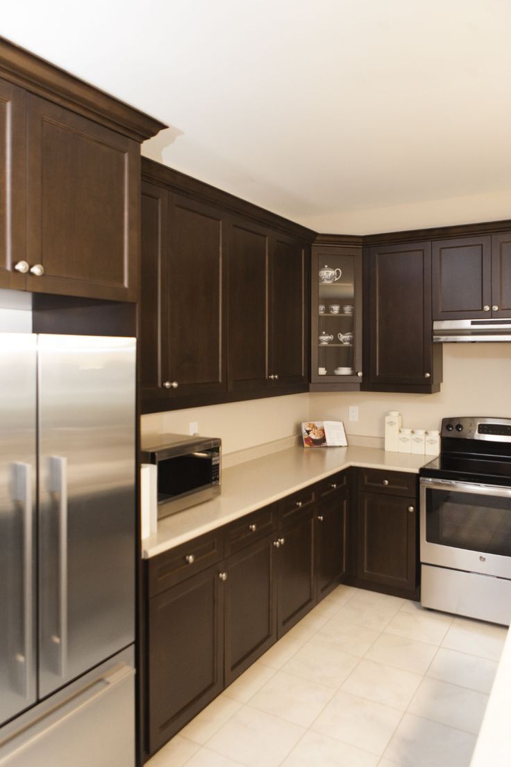 an empty kitchen with stainless steel appliances and brown cupboards on the walls, along with white tile flooring