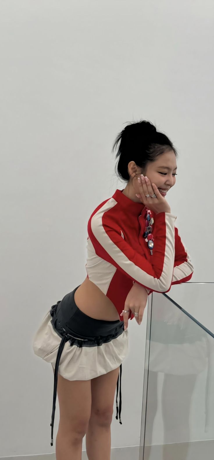 a woman in a red and white outfit talking on her cell phone while leaning against a glass railing