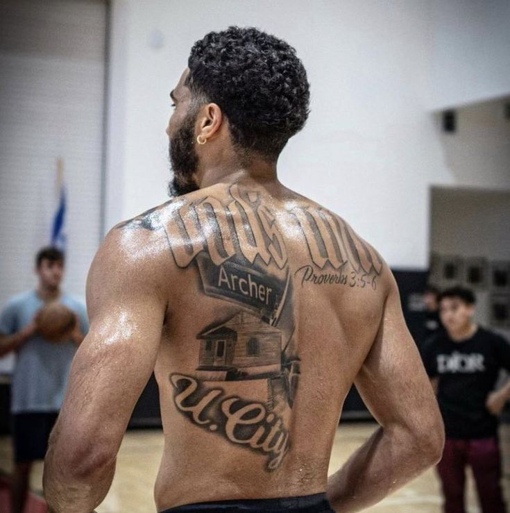 a man with tattoos on his back standing in front of a basketball court while others watch