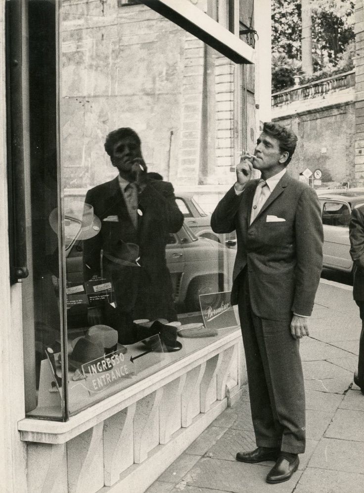 a man in a suit talking on a cell phone while standing next to a store window