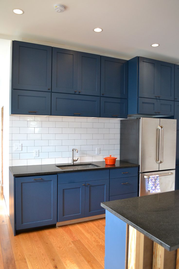 a kitchen with blue cabinets and white subway backsplash, stainless steel appliances and wood flooring