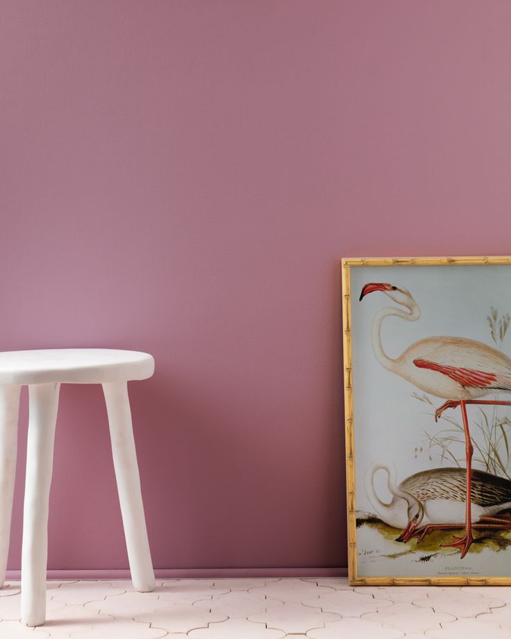 a white stool sitting next to a painting on a wall near a table and chair