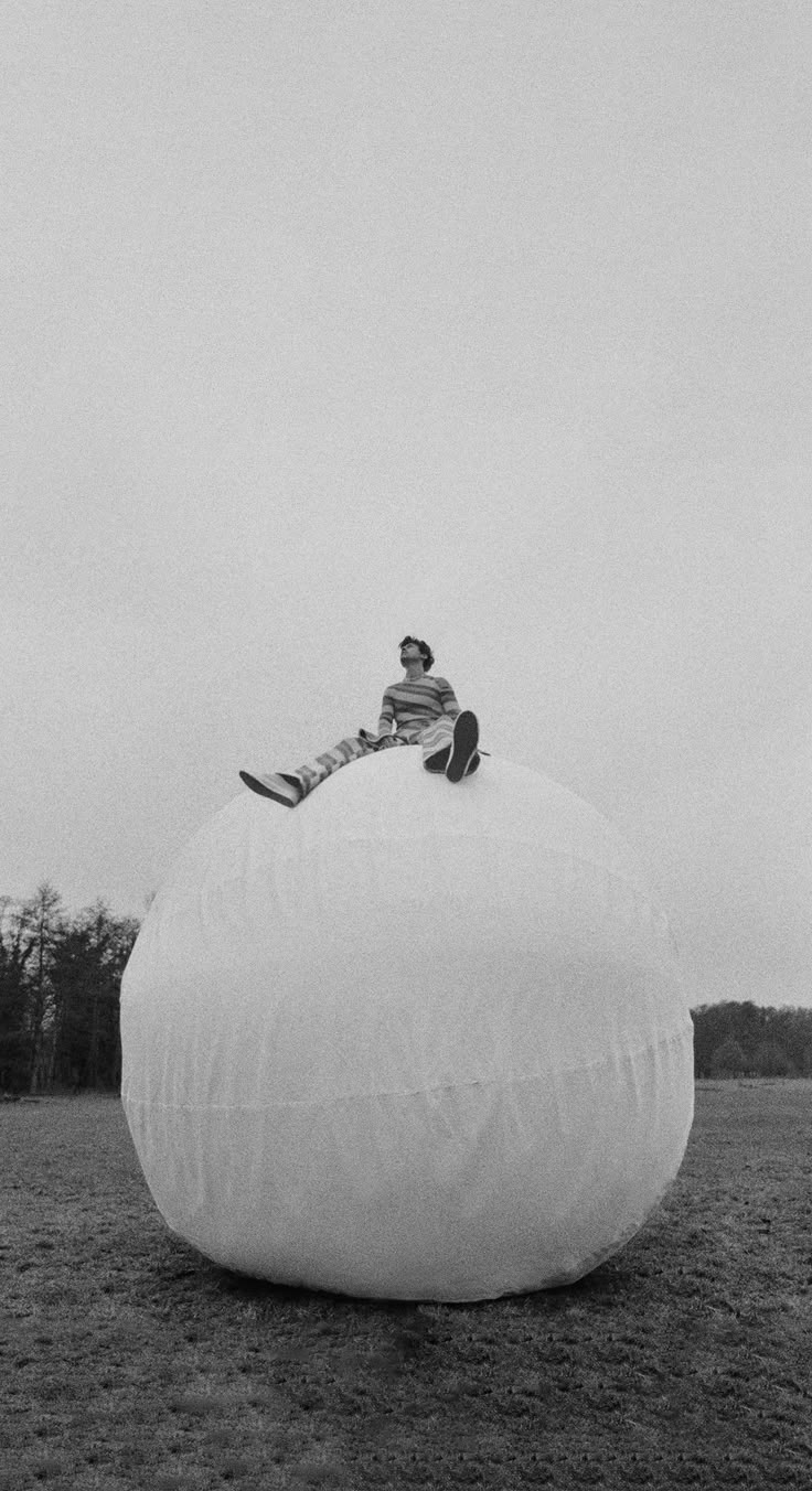 a man sitting on top of a large white ball in the middle of a field