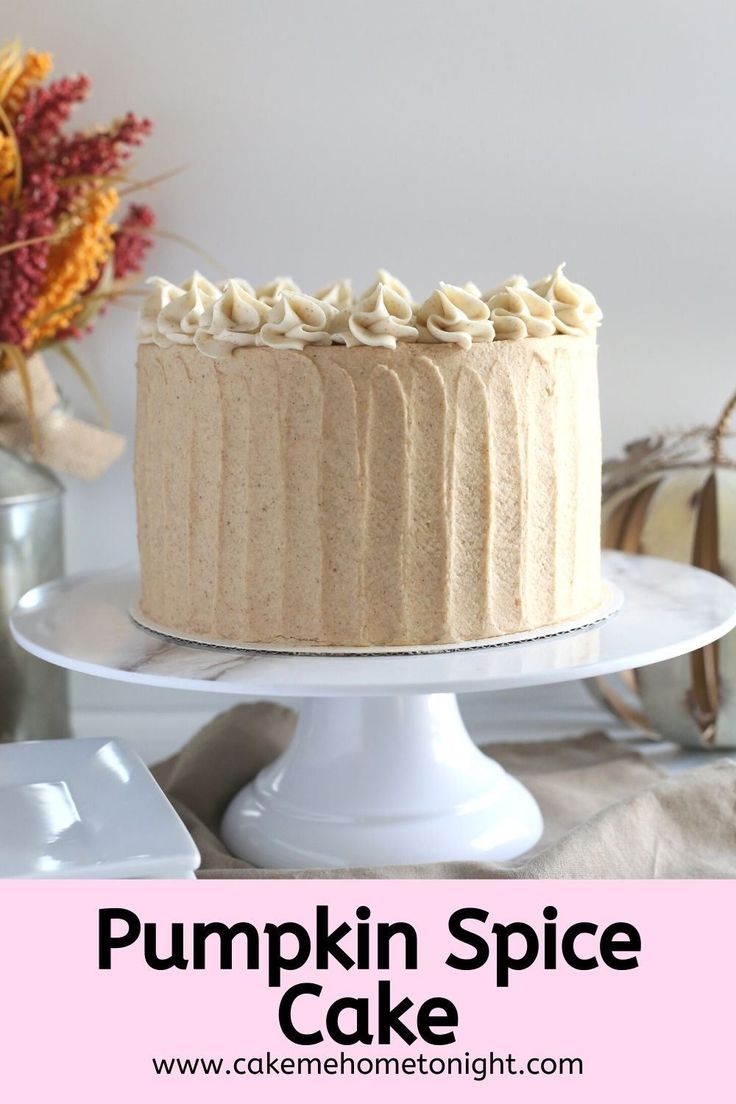 a pumpkin spice cake with frosting on a white cake platter next to fall decorations