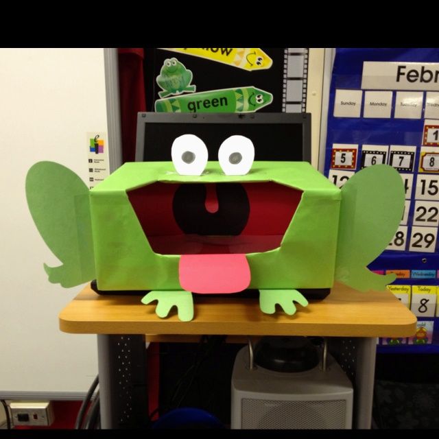 a green frog sitting on top of a wooden table next to a whiteboard with numbers