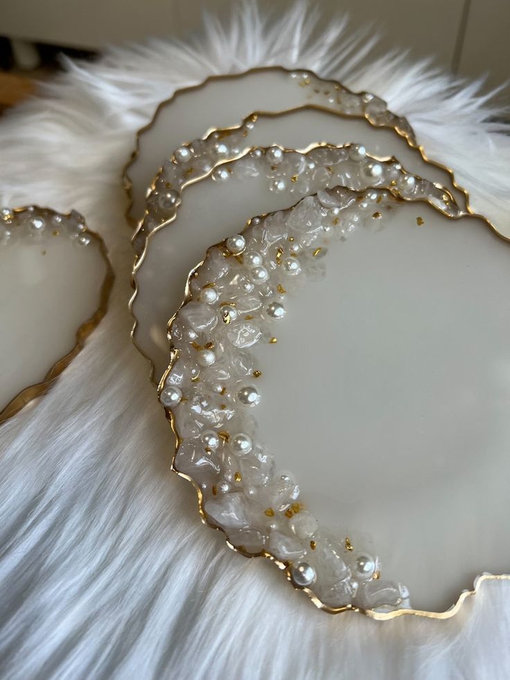 three white plates with gold trim and pearls on the edges, sitting on a fur surface