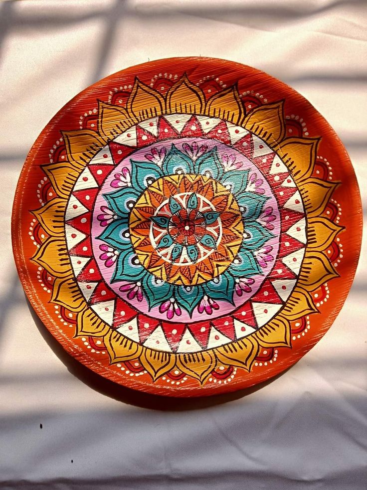 an orange plate with colorful designs on it sitting on a white tableclothed surface