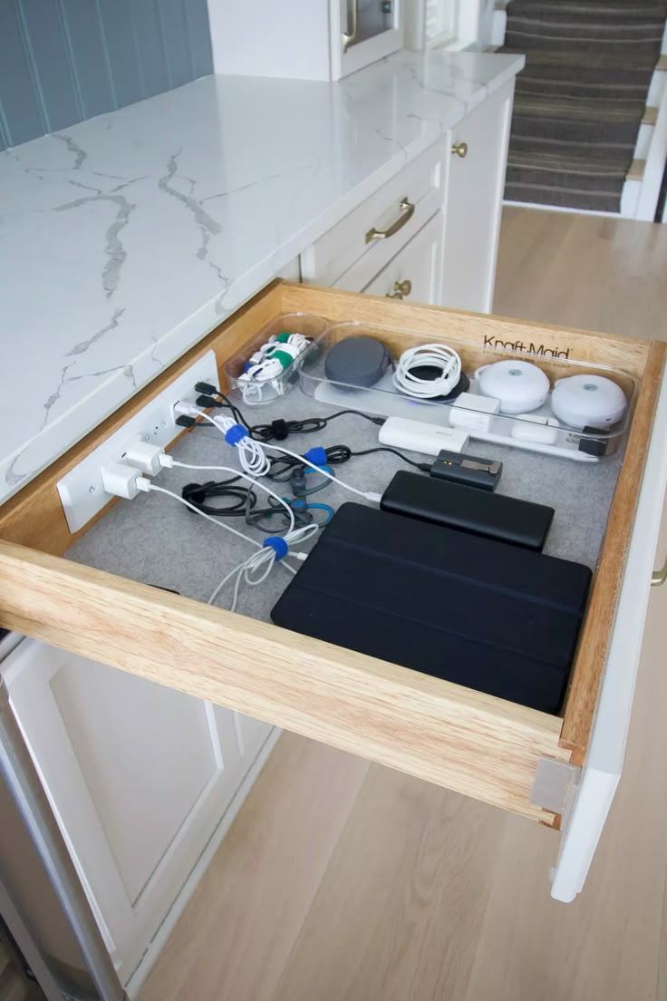 an open drawer in the middle of a kitchen counter with various items on it, including electronics and cords