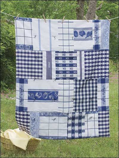 a blue and white quilt hanging on a clothes line in the grass with a basket next to it