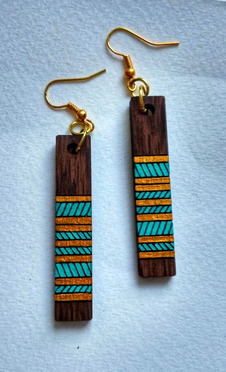 two wooden earrings with blue and green designs on them, hanging from gold earwires