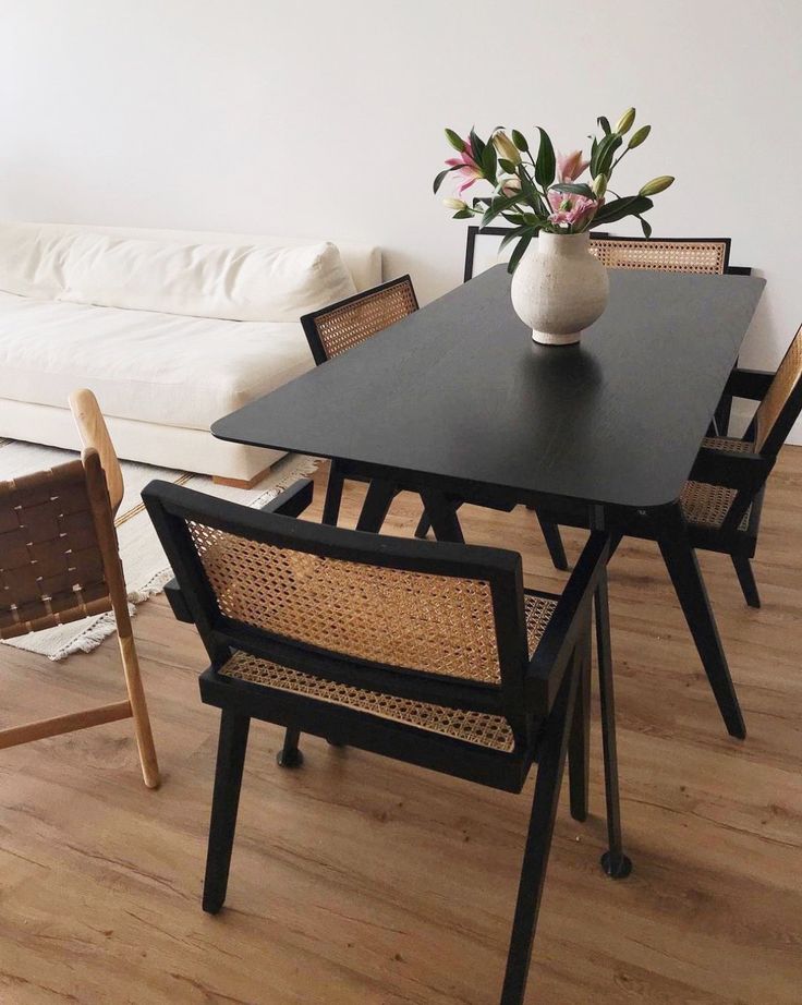 a black table with chairs and a vase on it in front of a white couch