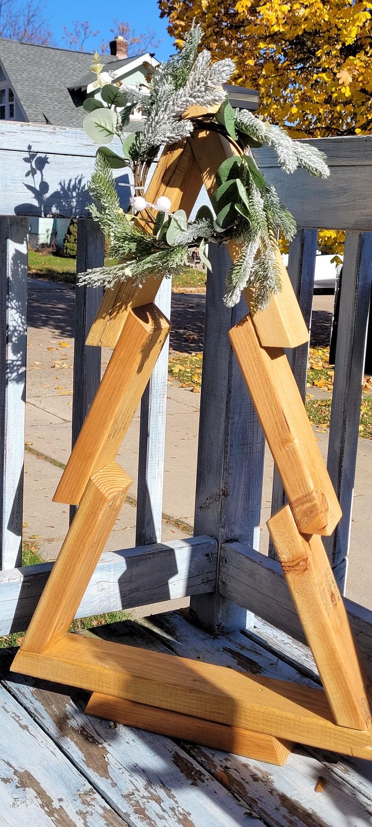 a wooden triangle with greenery on it sitting on a porch next to a fence