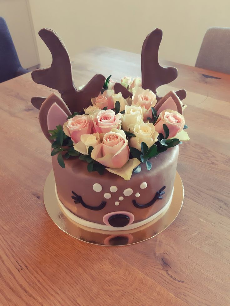 a chocolate cake with flowers and deer antlers on it's head sitting on a wooden table