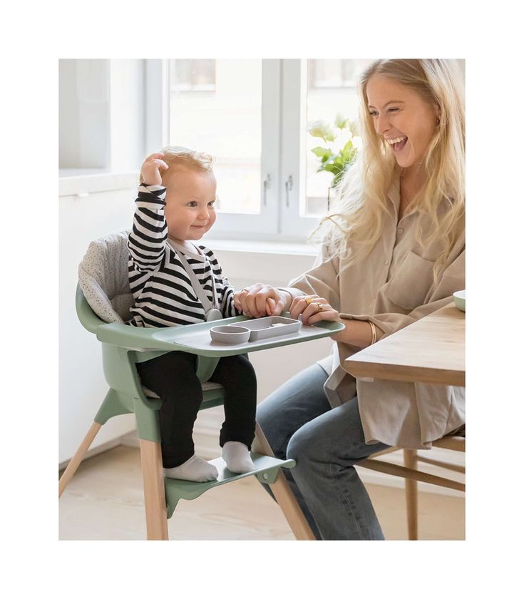 a woman sitting at a table with a baby in a high chair